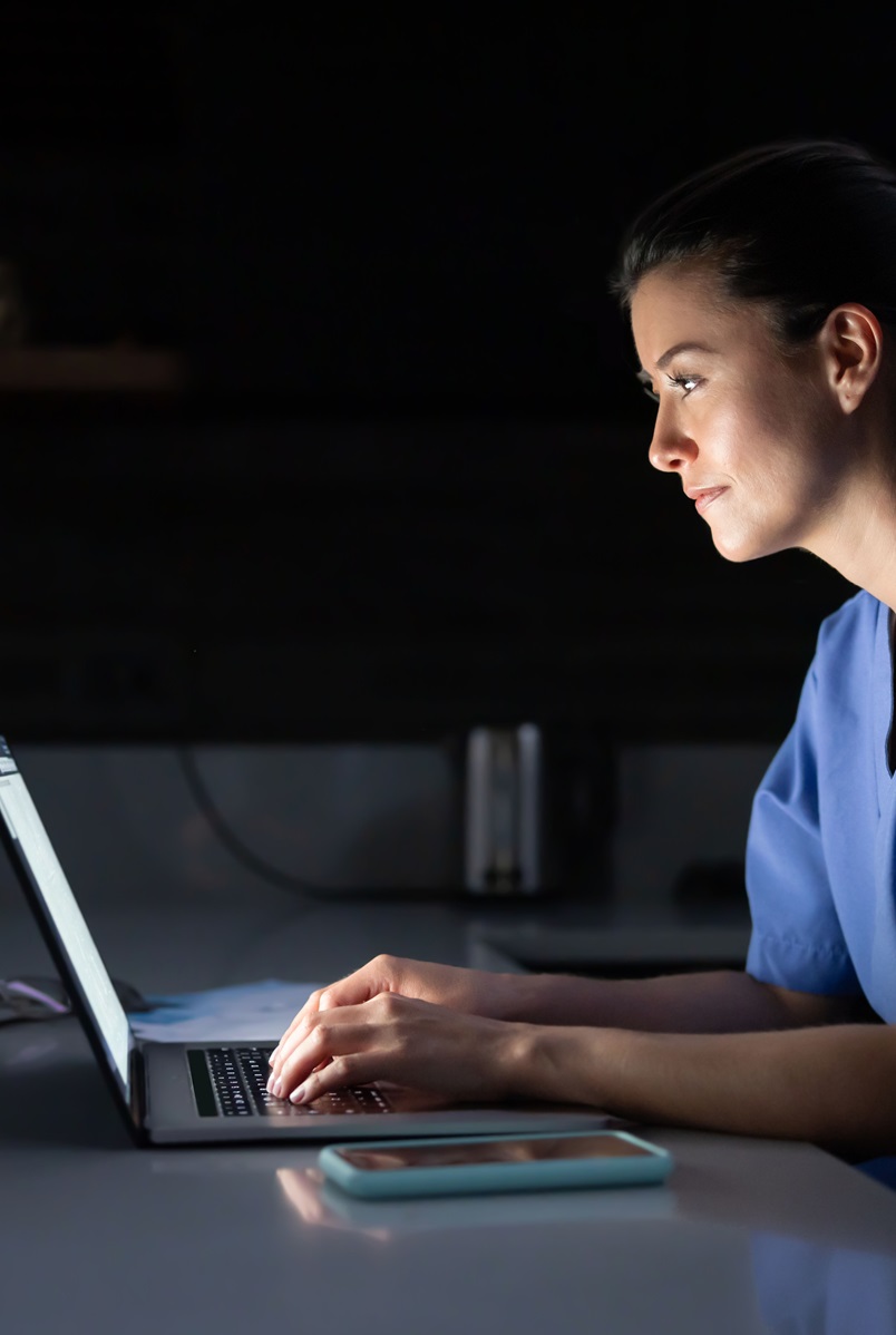 young woman in scrubs typing on a laptop