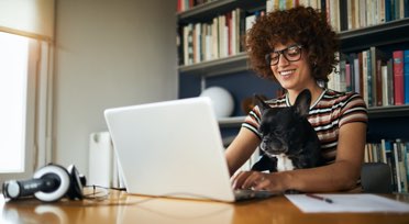 Female student learning on laptop at home with dog on lap