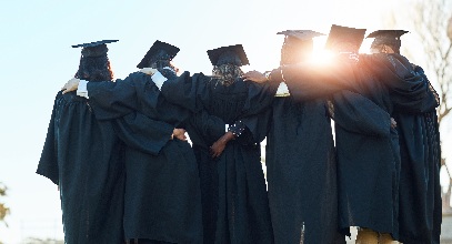 6 recent graduates holding onto each other all while still wearing their caps and gowns with the sun rays shining