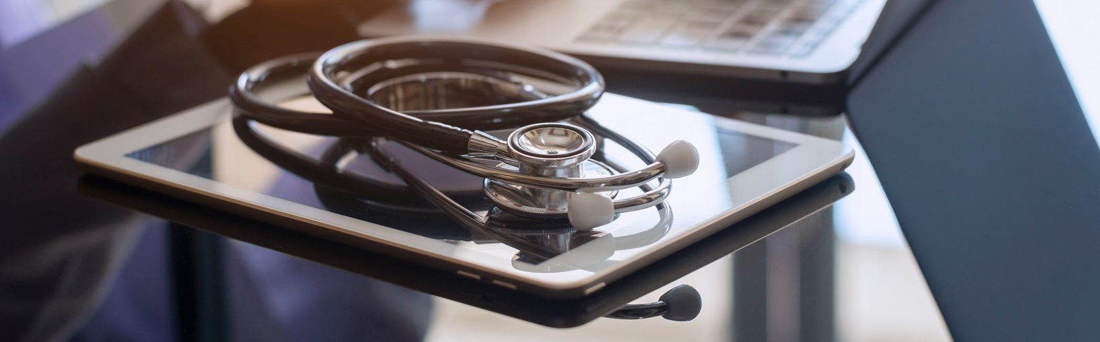 stethoscope and a tablet next to the laptop on a table