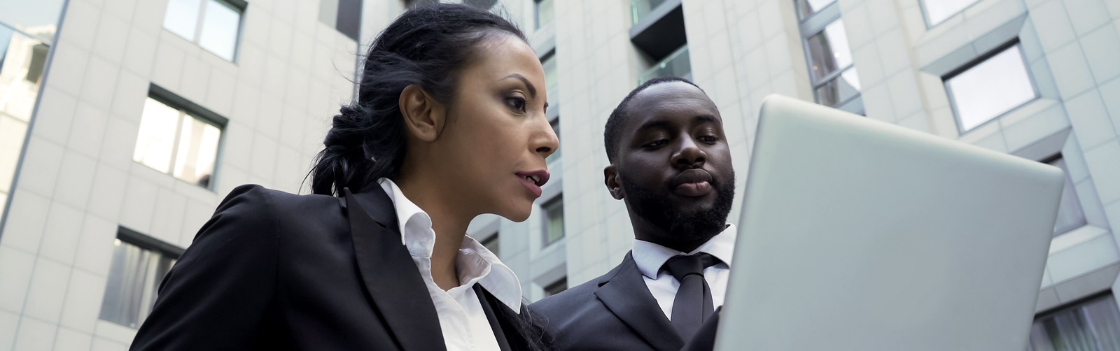 an african american woman and man conversing outside a building looking at the screen of a laptop