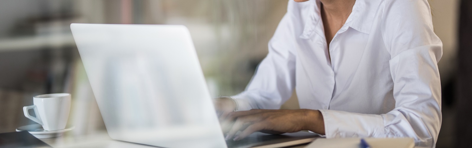 woman sitting at a desk with a coffee cup typing on her laptop