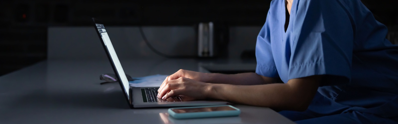 young woman in scrubs typing on a laptop