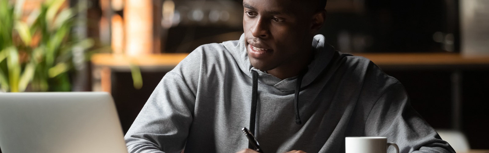 African American man sitting at a desk with a computer, pen and paper, and coffee mug (very self aware)