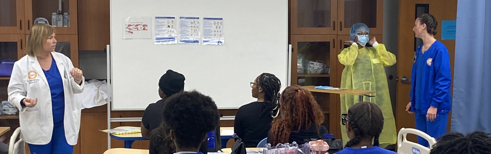 group of high school students in scrubs listening to a presentation by several healthcare professionals