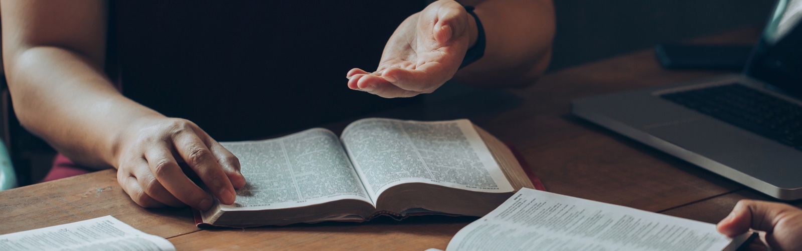 three people gathered around a table discussing theology