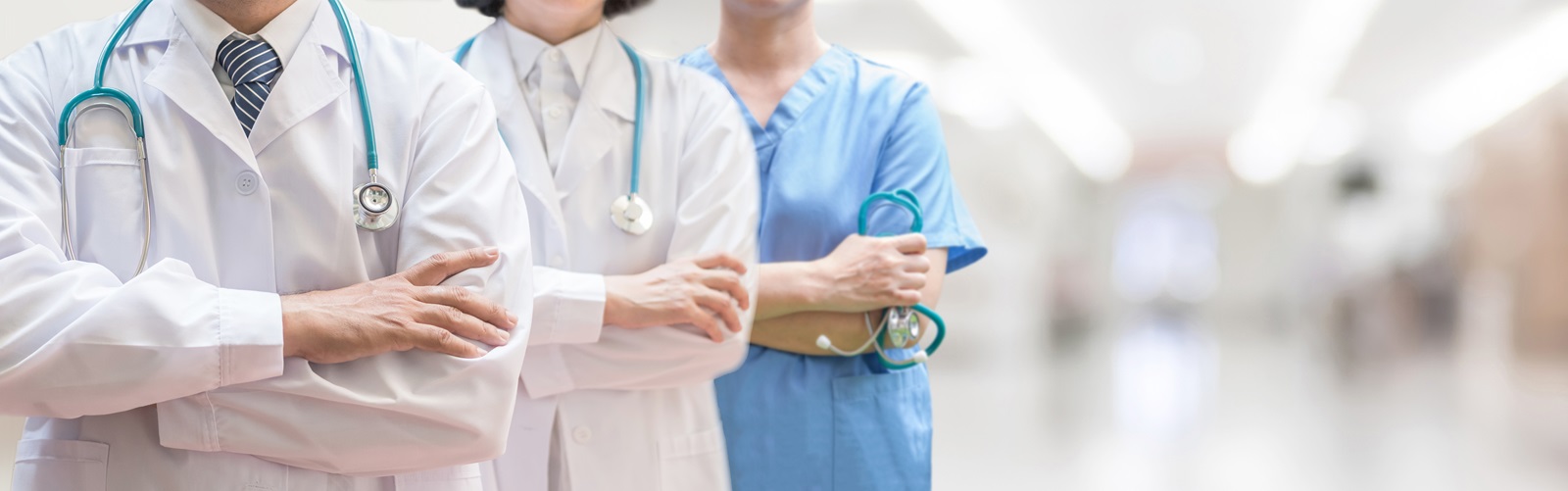 three hospital professionals, one man and two women, standing in a hallway holding their stethescopes