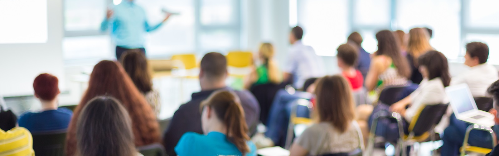 variety of adults sitting in a class room listening to an instructor give a presentation