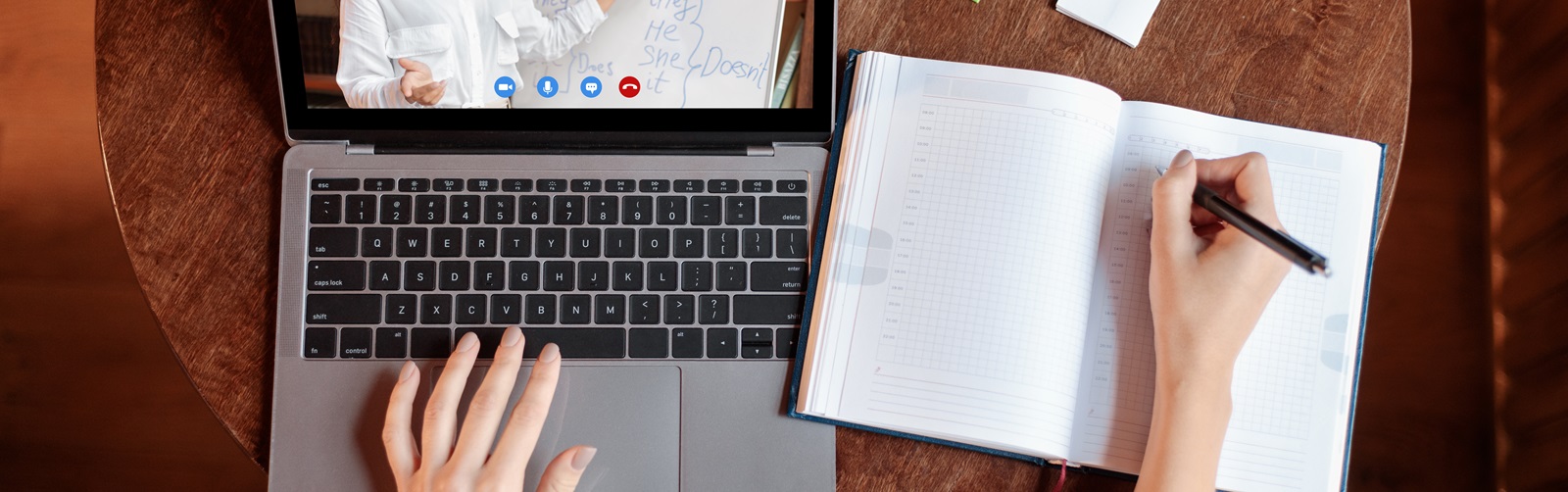 person sitting at a desk watching a video on a laptop writing in a notebook