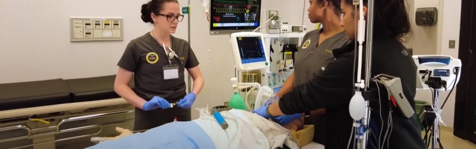 three female st;udents in a hospital room practicing on a dummy