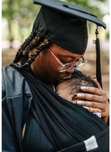 Szhanesha Becoat, and her baby, in a wooded park in her cap and gown