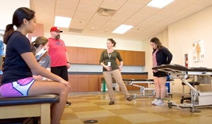 group of men and women students listening to an instructor in a physical therapy classroom