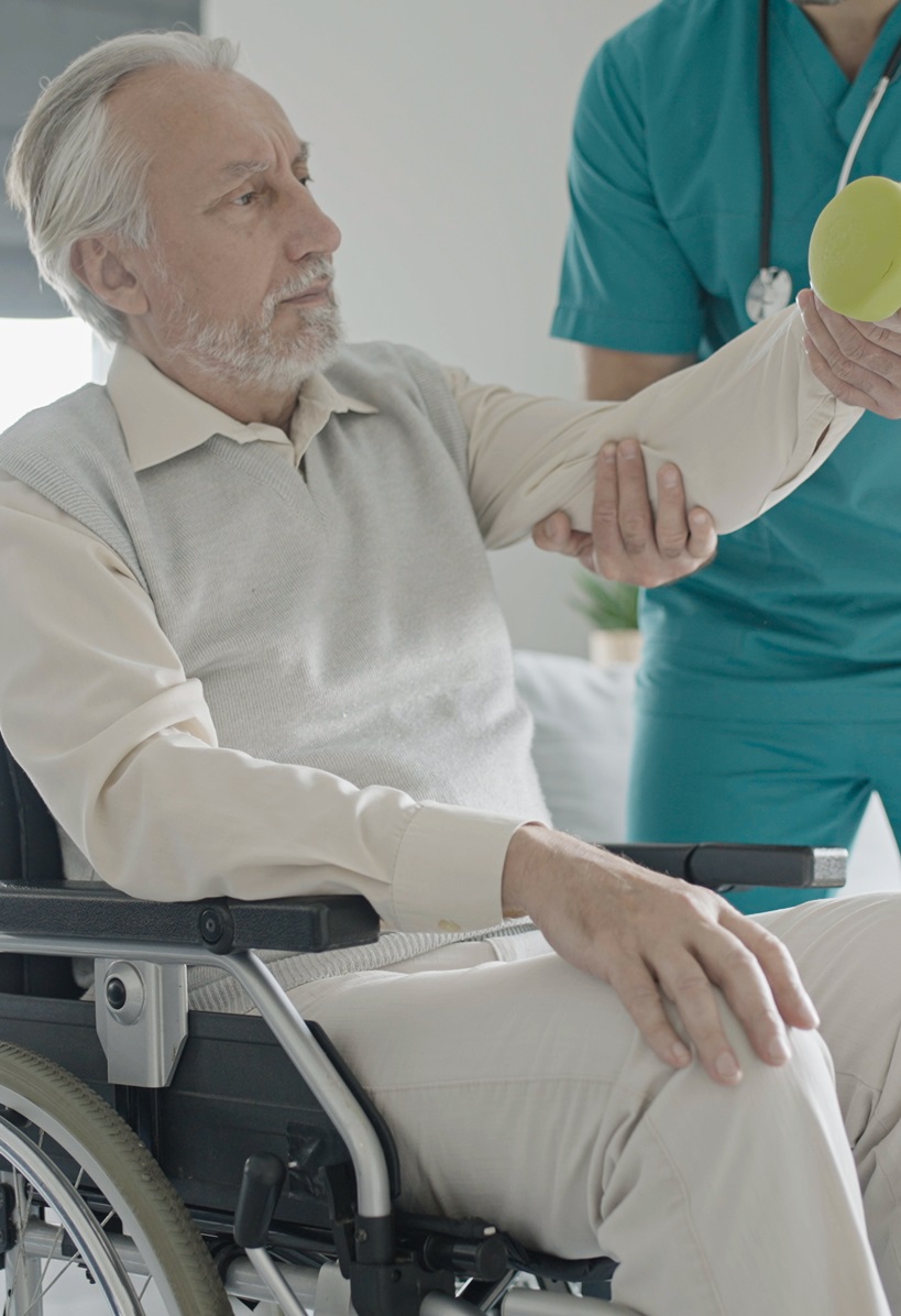 older gentleman sitting in a wheelchair receiving help with weight lifting from physical therapy assistant