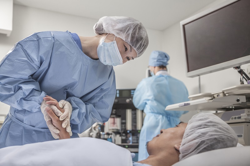 Anesthesiologist assistant in scrubs comforting a patient on a hospital bed