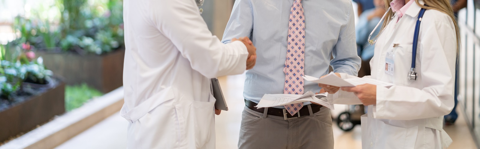 two male and one female healthcare worker discussing paperwork in a hospital hall