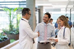 two male and one female healthcare worker discussing paperwork in a hospital hall