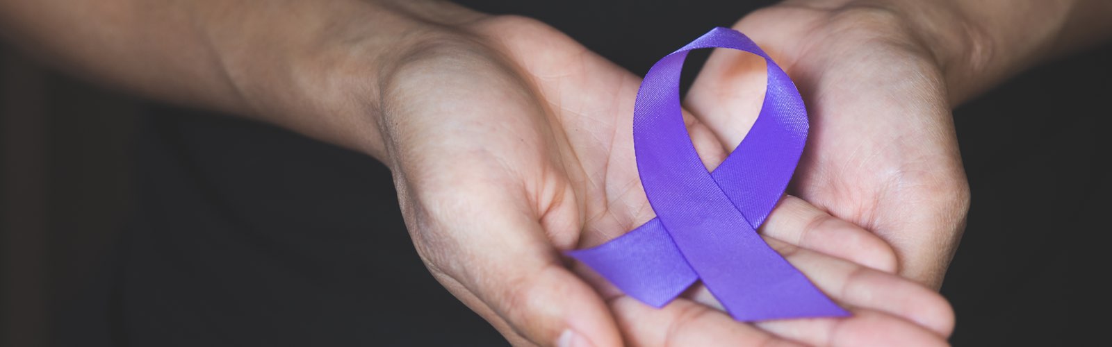 Two hands holding Domestic Violence Awareness Month purple ribbon