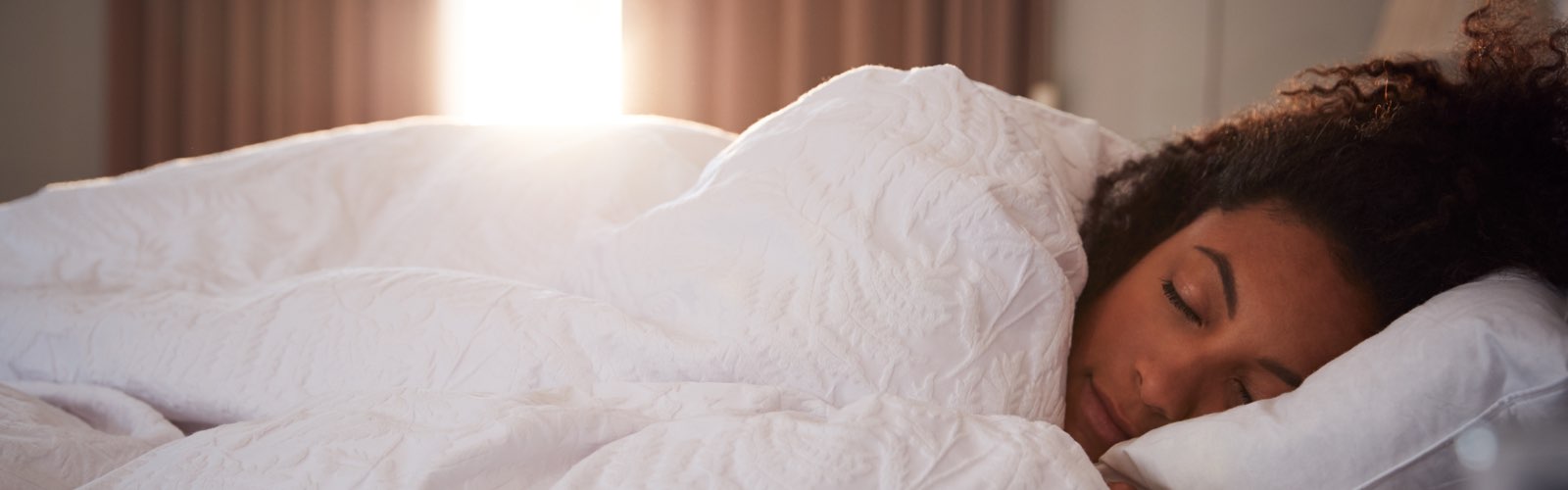 Young woman sleeping in bed as sun rises