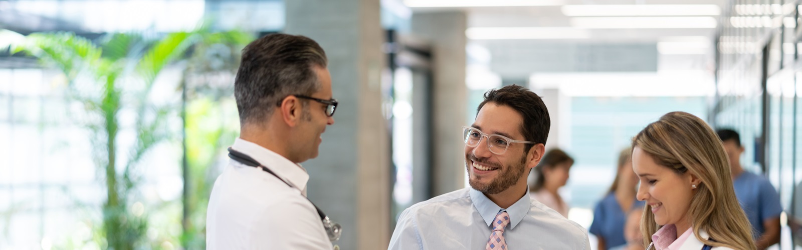 2 male doctors and 1 female doctor discussing healthcare items in a hallway