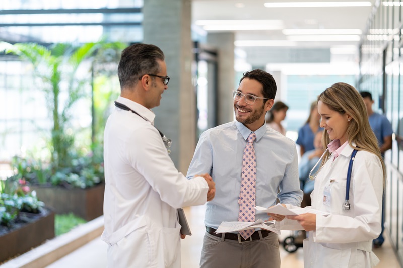 2 male doctors and 1 female doctor discussing healthcare items in a hallway