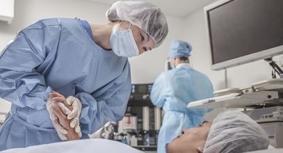 female healthcare worker in blue surgery scrubs holding the hand of a male patient laying down on a table