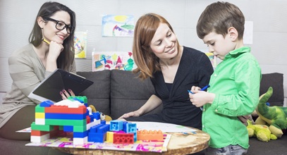 female counselor supervising a mom and her son while they play together with blocks at a table