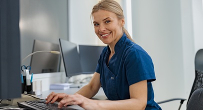 blonde woman sitting at a desk typing at a computer wearing a blue shirt