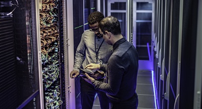 two men standing in a server room looking at a tablet