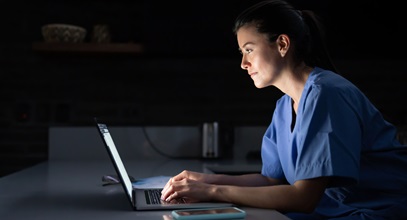 young woman in scrubs typing on a laptop